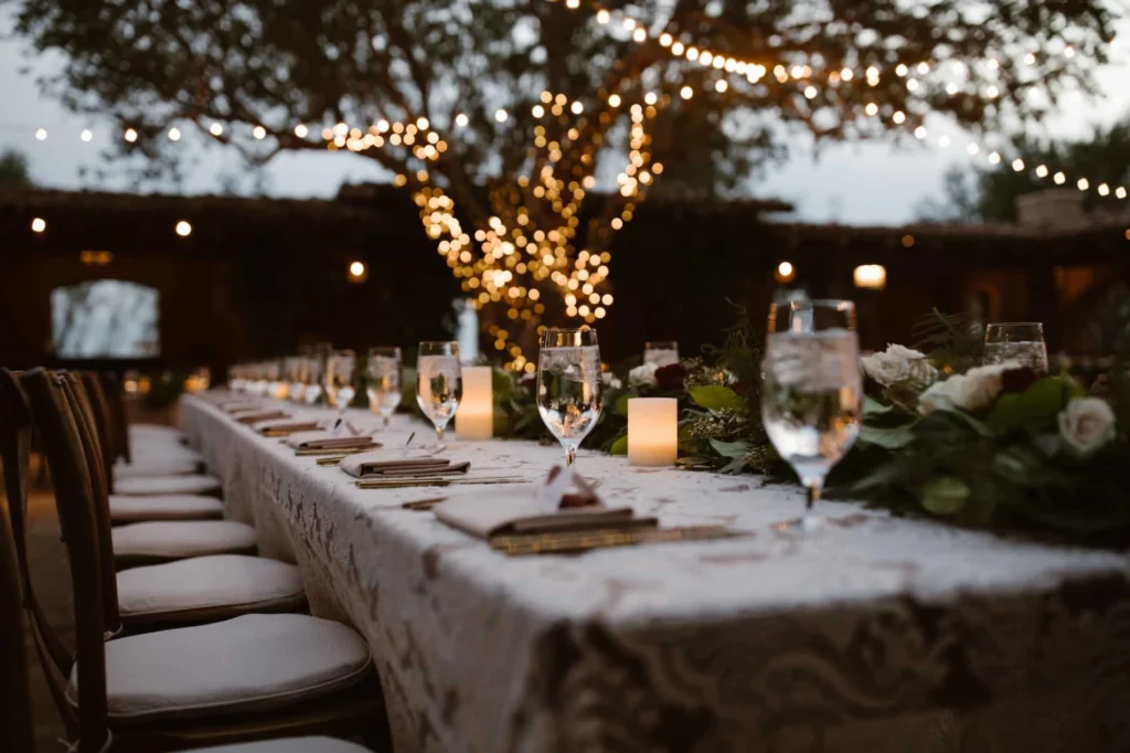 table at wedding with lit up tree in the background and string lights